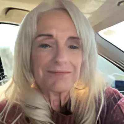 A woman with long white hair sitting in the back of a car.